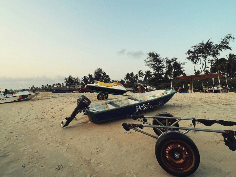 A view of a boat with a motor attached to it, a jet ski behind it on the shoreline of Varca Beach and trees in the background.