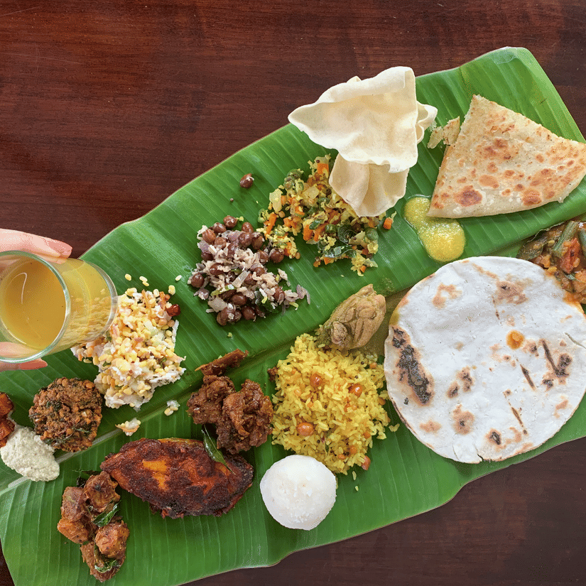 A sadhya on a banana leaf featuring various dishes and a drink