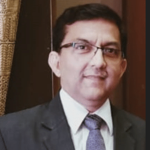  Vinay Kumar Singh wearing a dark suit, light shirt, and a purple tie, standing indoors