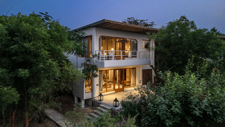 Exterior facade of a Forest villa surrounded by plants and trees during twilight hour with the lights on inside the villa at Utsav Camp Sariska.