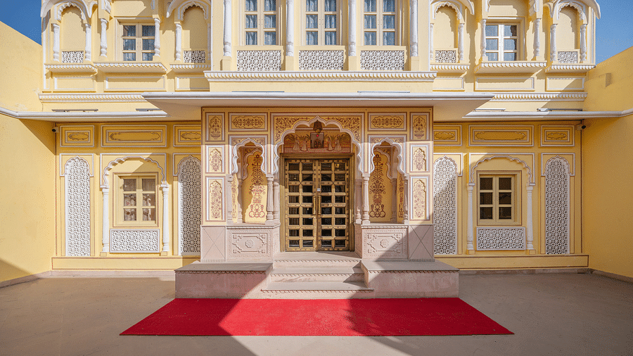 entrance of the hotel with intricate wall paintings along with a red carpet in front of it - Brij Castle, Jaipur