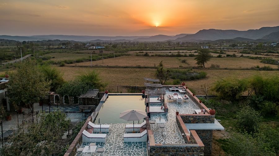 An image of a seating arrangement near the swimming pool in the open with the backdrop of sunset - Utsav Camp Sariska