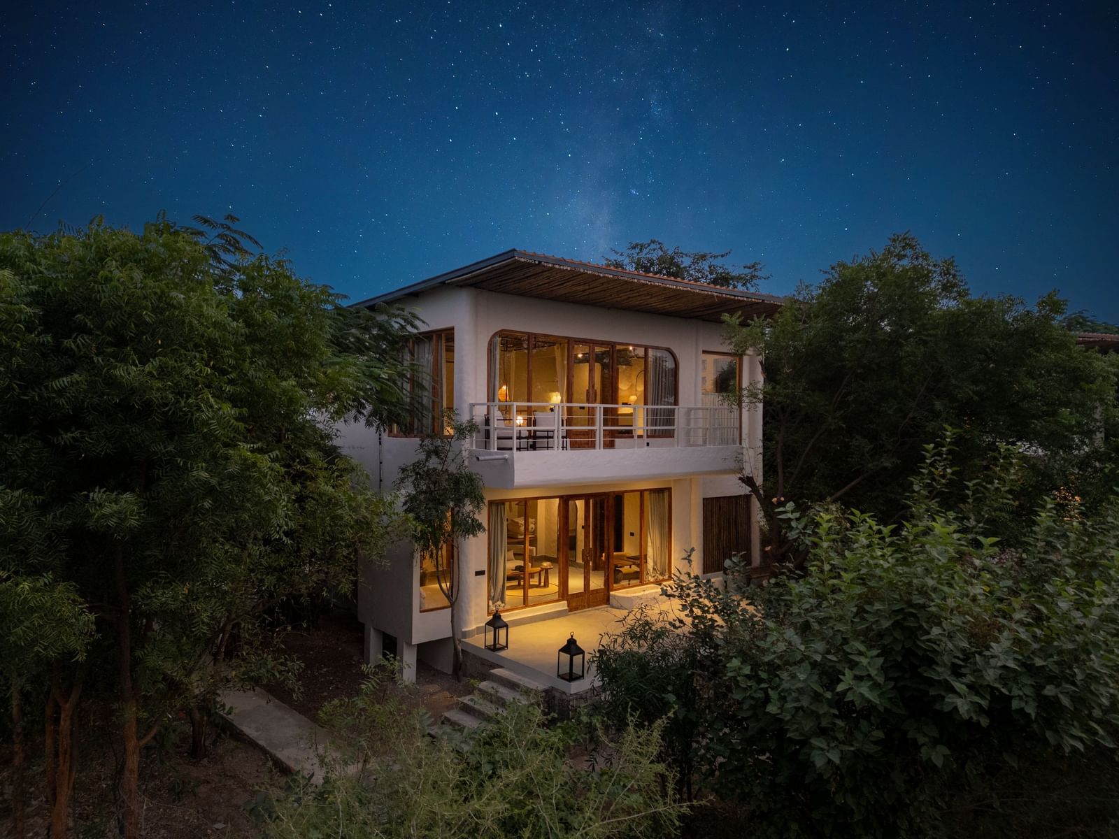 Exterior of a modern two-story villa surrounded by trees and plants.