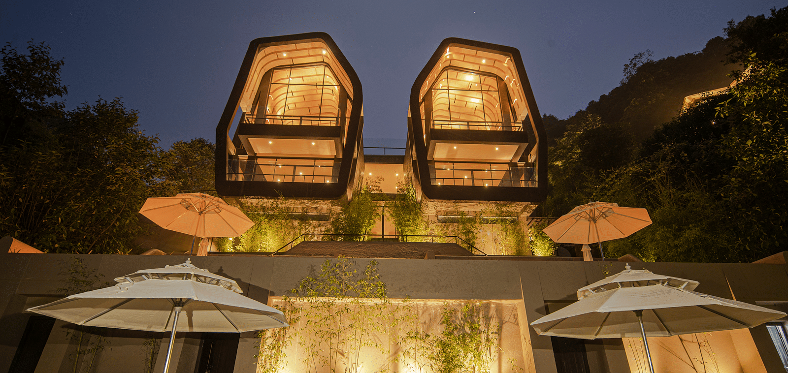 A front view of two individual beautifully lighted villas | A bedroom with large window giving a view of a sitting area on the deck | Kavya Resort and Spa, Nagarkot