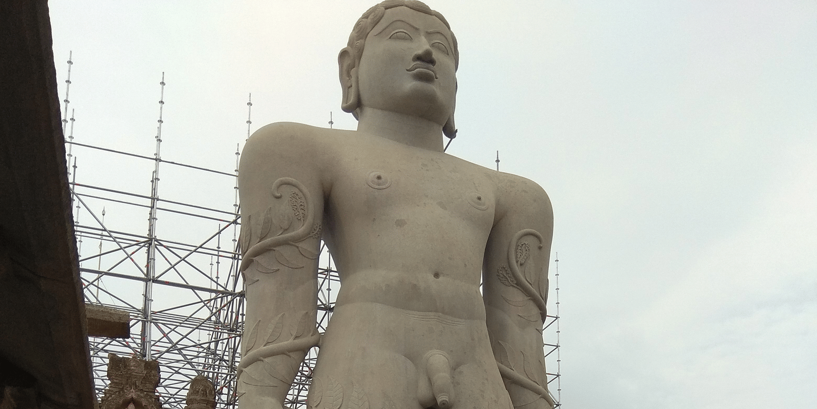 A giant statue of Gommattesvara in Shravanabelagola (Karnataka) under a clear sky with people walking around.
