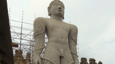A giant statue of Gommattesvara in Shravanabelagola (Karnataka) under a clear sky with people walking around.