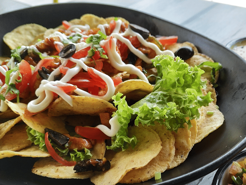 A dark plate of tortilla chips topped with tomatoes, olives, lettuce and a drizzle of sauce