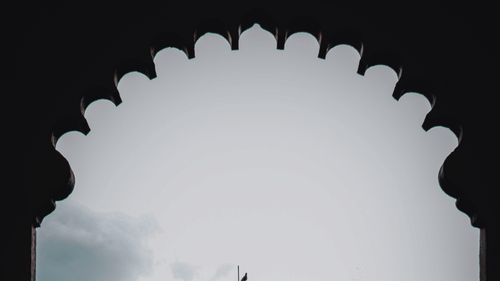 A building with a dome seen through an arched doorway with clear blue sky in the background.