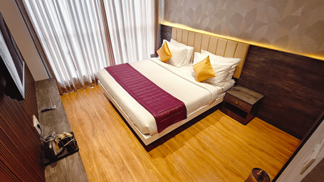 A double bed with white linens and a maroon runner sits on a light wood floor in a room with wood-panelled walls at Bliss Casa Mila By Bergamont Hotels, Kodaikanal.