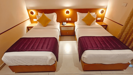 A twin-bedded room at Bliss Giriya By Bergamont Tiruvannamalai with wooden headboards, reading lights, and an angled ceiling.