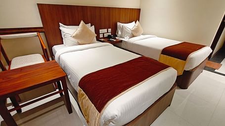Twin-bed room at Hotel Alps Residency, Krishnagiri, with crisp white linens and warm wooden accents.