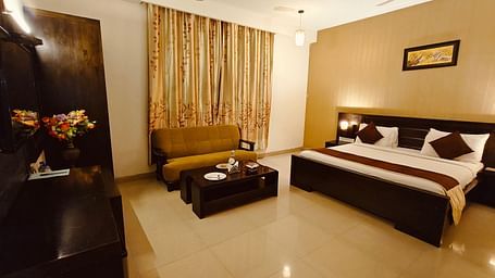 Suite with king size bed room with sofa, side tables, and warm lighting at Hotel Alps Residency, Krishnagiri.