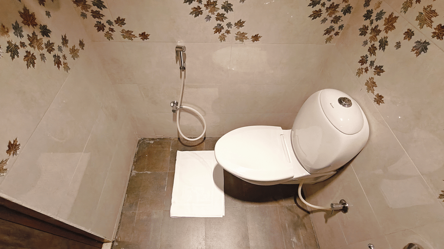 A white ceramic toilet is mounted on a wall with brown and white leaf-patterned tiles at Bliss Casa Mila By Bergamont Hotels, Kodaikanal.