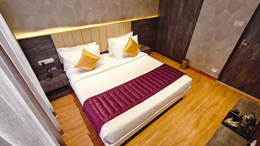 A double bed with a purple bed runner and gold cushions seen from a high angle on a wooden floor at Bliss Casa Mila By Bergamont Hotels, Kodaikanal.