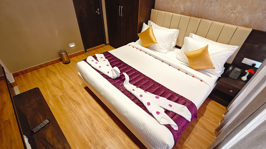 A large bed with white linens, a purple runner, and towels folded into a swan shape at Bliss Casa Mila By Bergamont Hotels, Kodaikanal.