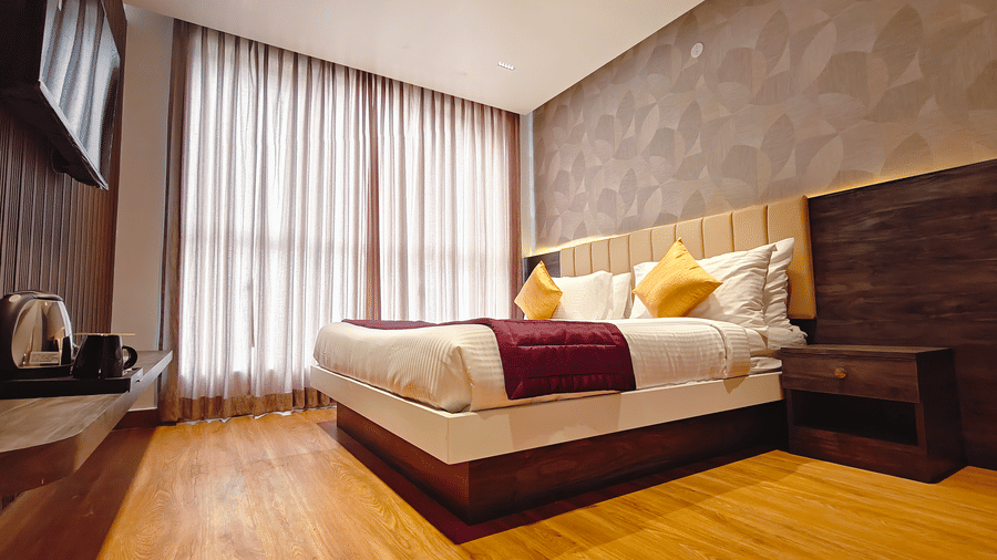 A double bed with a maroon runner faces a wall-mounted television in a room with patterned wallpaper at Bliss Casa Mila By Bergamont Hotels, Kodaikanal.