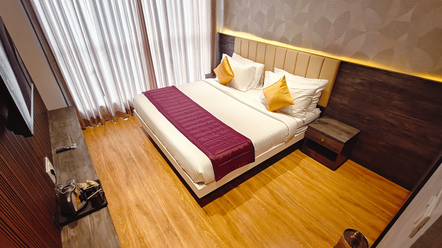 A double bed with white linens and a maroon runner sits on a light wood floor in a room with wood-panelled walls at Bliss Casa Mila By Bergamont Hotels, Kodaikanal.