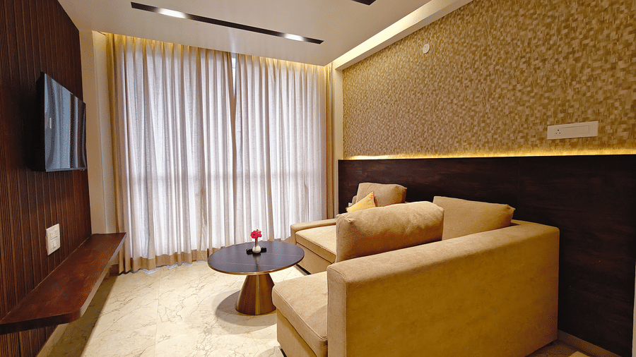 A beige sofa and a black coffee table are set in a room with wood-panelled walls and curtains at Bliss Casa Mila By Bergamont Hotels, Kodaikanal.