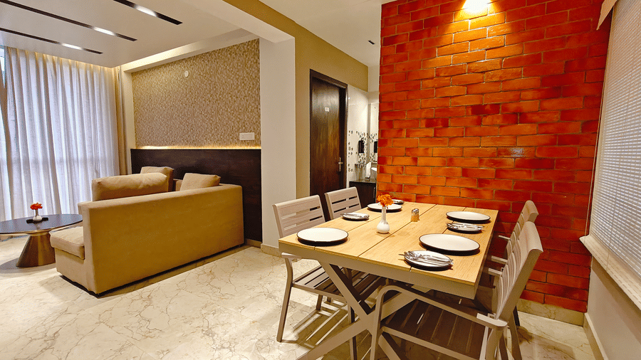 A wooden dining table with 4 chairs set next to a textured red brick wall in a hotel suite at Bliss Casa Mila By Bergamont Hotels, Kodaikanal.