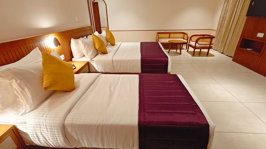 A family room at Bliss Giriya By Bergamont Tiruvannamalai with three beds, wooden headboards, and wicker seating.