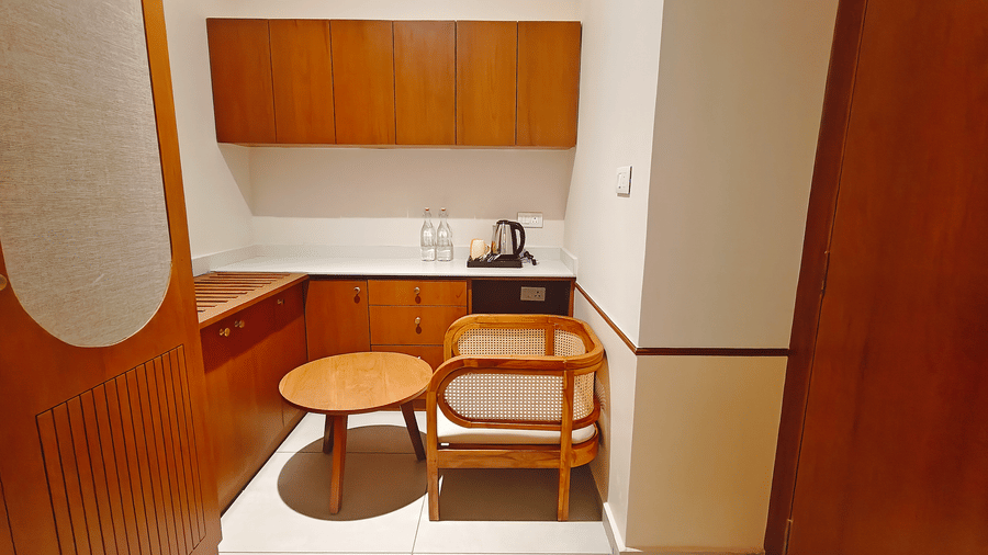 A wooden kitchenette and work area at Bliss Giriya By Bergamont Tiruvannamalai with built-in cabinetry, a table, and a chair.