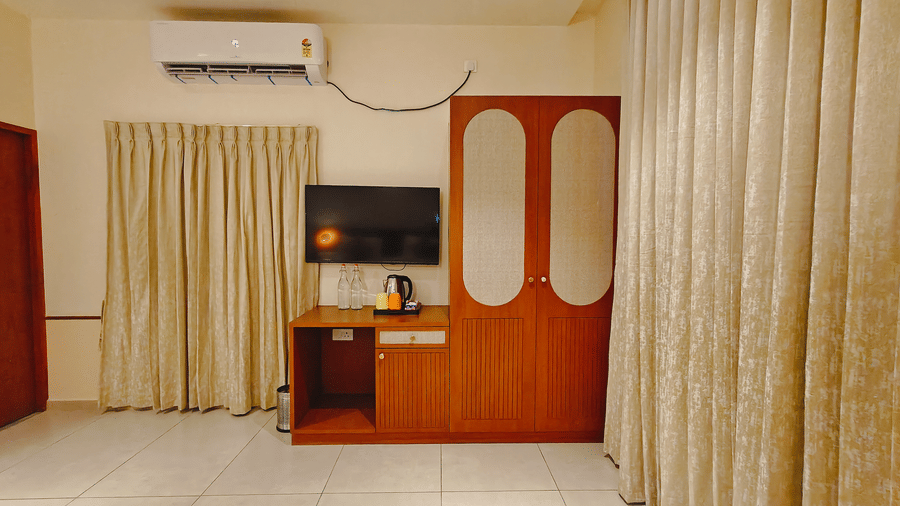 A hotel room at Bliss Giriya By Bergamont Tiruvannamalai with a wall-mounted television, air conditioning unit, and draped windows.