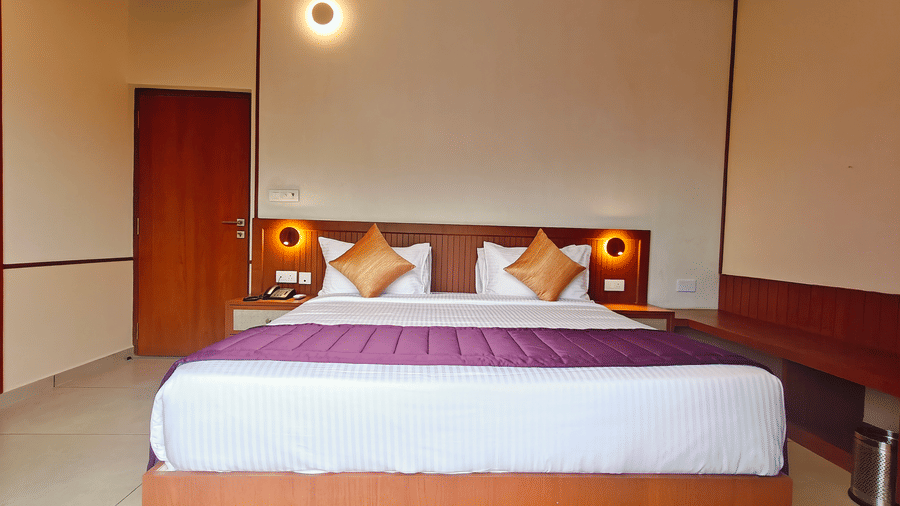 A double bed with a wooden panel headboard and wall-mounted reading lights at Bliss Giriya By Bergamont Tiruvannamalai.