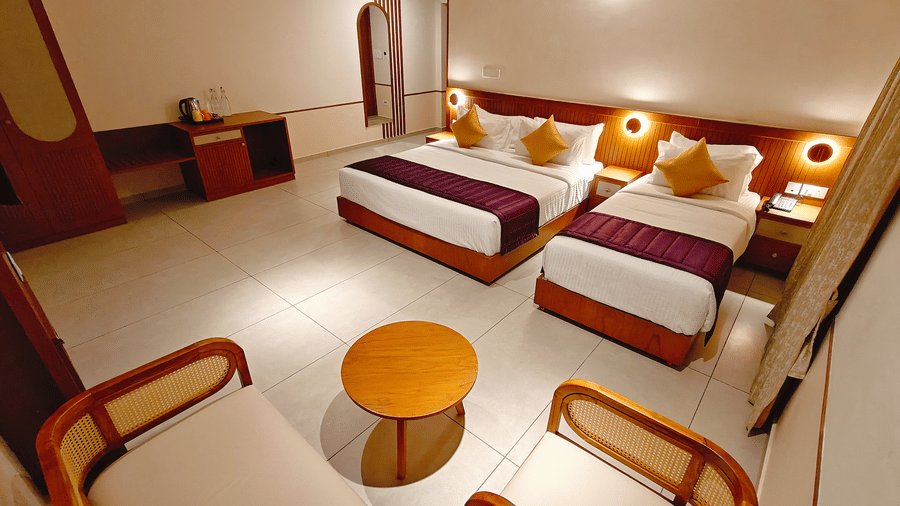 A wide-angle view of a twin-bedded room at Bliss Giriya By Bergamont Tiruvannamalai with wooden chairs and a round side table.