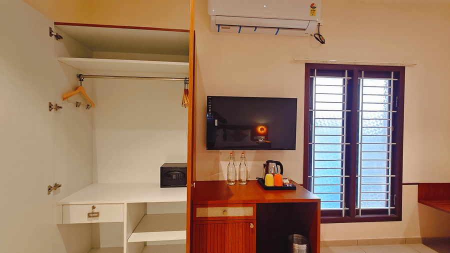 A compact work desk and wall-mounted television in a room at Bliss Giriya By Bergamont Tiruvannamalai with louvred windows.