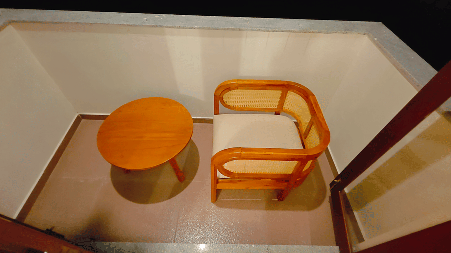 A close-up of a wooden armchair and round side table in a room at Bliss Giriya By Bergamont Tiruvannamalai.