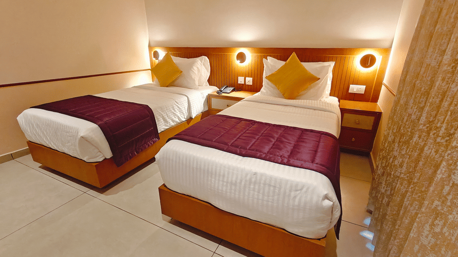 A neatly made single bed with a wooden headboard and wall-mounted reading lights at Bliss Giriya By Bergamont Tiruvannamalai.