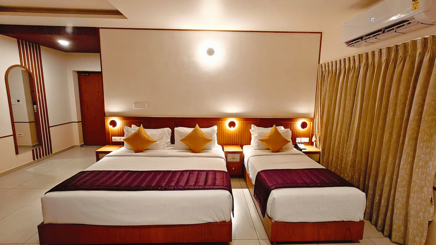 A twin-bedded room at Bliss Giriya By Bergamont Tiruvannamalai with wooden headboards, an air conditioning unit, and draped curtains.