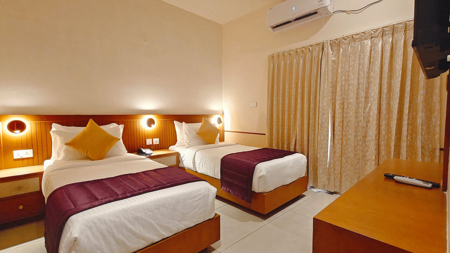 A twin-bedded room at Bliss Giriya By Bergamont Tiruvannamalai with wooden headboards, reading lights, and floor-length curtains.