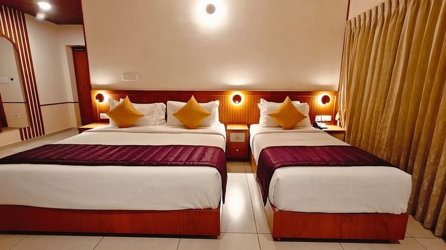 A twin-bedded room at Bliss Giriya By Bergamont Tiruvannamalai with wooden headboards, reading lights, and draped curtains.