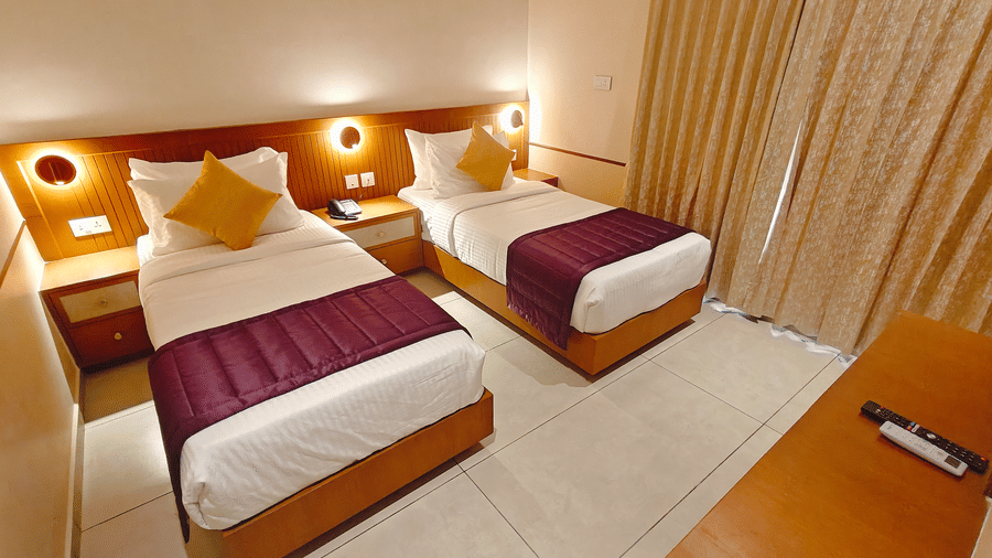A side-angle view of a twin-bedded room at Bliss Giriya By Bergamont Tiruvannamalai with wooden headboards and draped curtains.