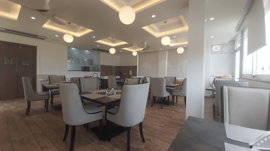 Indoor dining area of the Panther's Perch restaurant in Ramnagar with grey-coloured cushioned chairs surrounding the dining tables at Eminence The Corbett - Best resort in Nainital