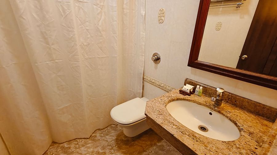Bathroom with shower curtain, WC, and wash basin in beige tiles at Hotel Alps Residency, Krishnagiri.