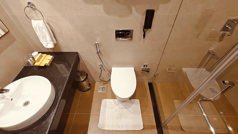 MM Legacy, Kanchipuram | A bathroom with a toilet seat, towels, and other toileteries.