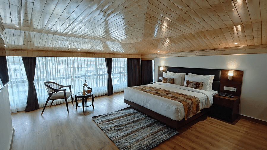 A bed with white linens and a patterned runner, a chair and a small table by the window, in a room with a wood ceiling - Sumitel JB Park, Darjeeling