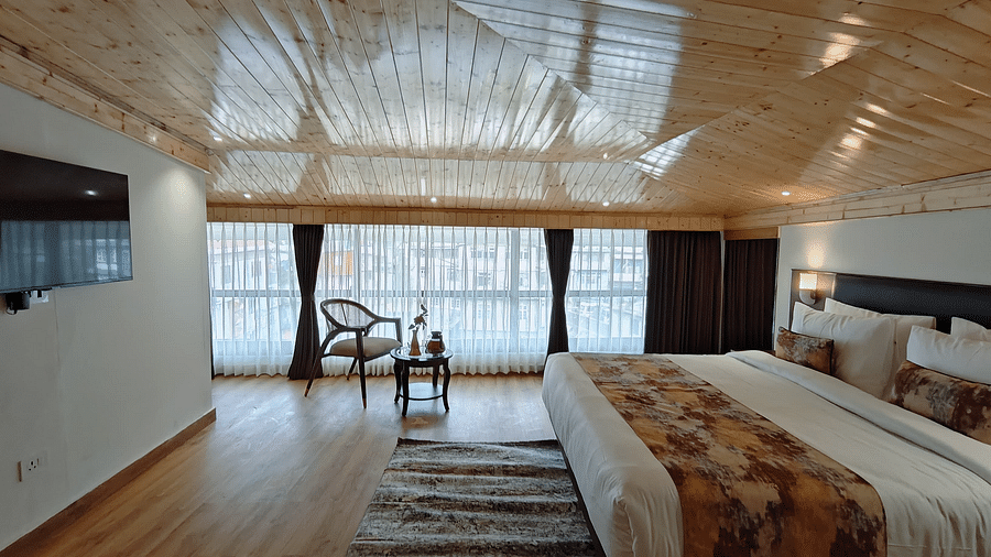 A wide angle of a hotel room with a bed, tv, a chair and a view through a window, showing a clean and modern design - Sumitel JB Park, Darjeeling