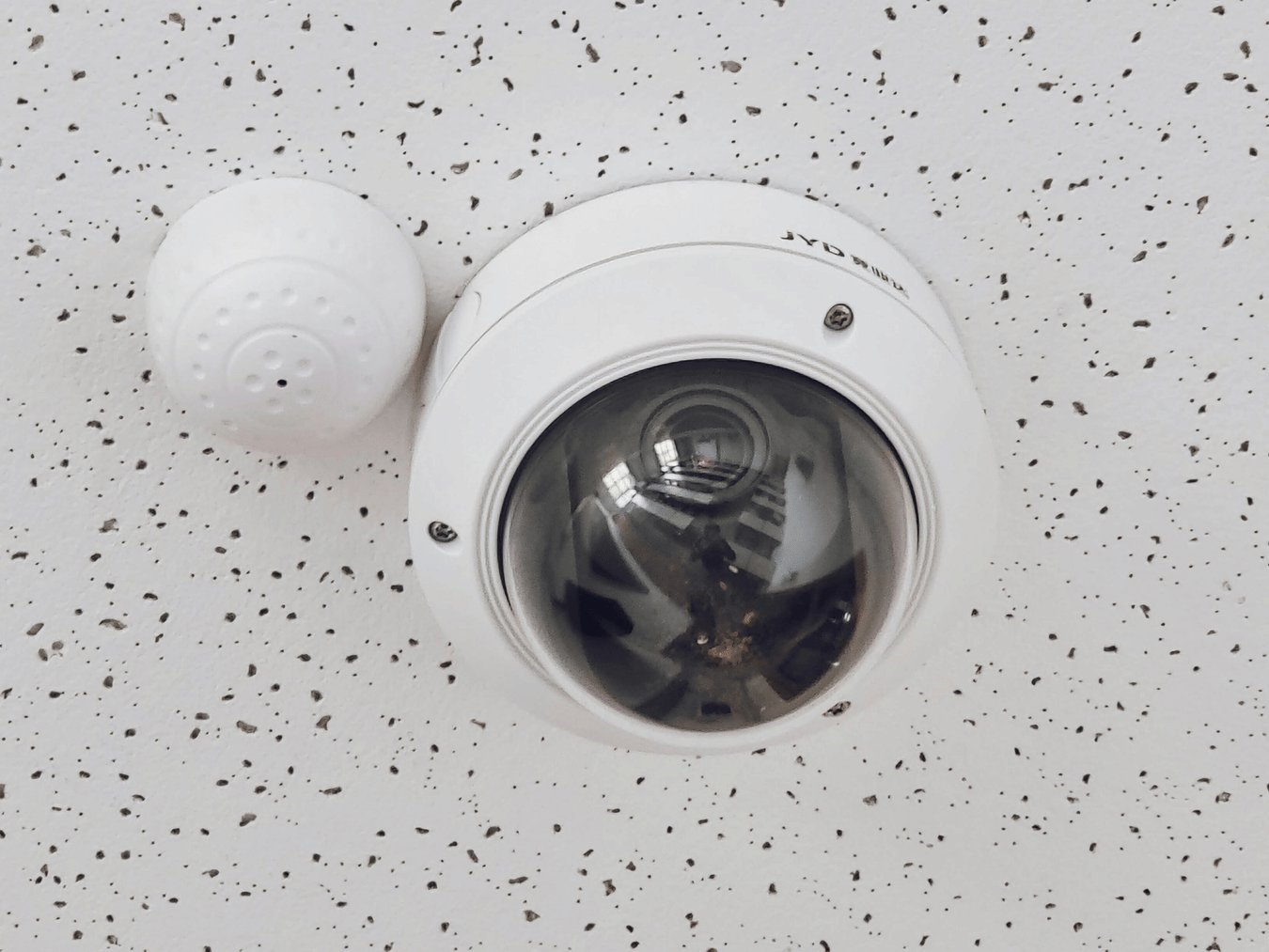 Dome security camera installed on a speckled white ceiling.