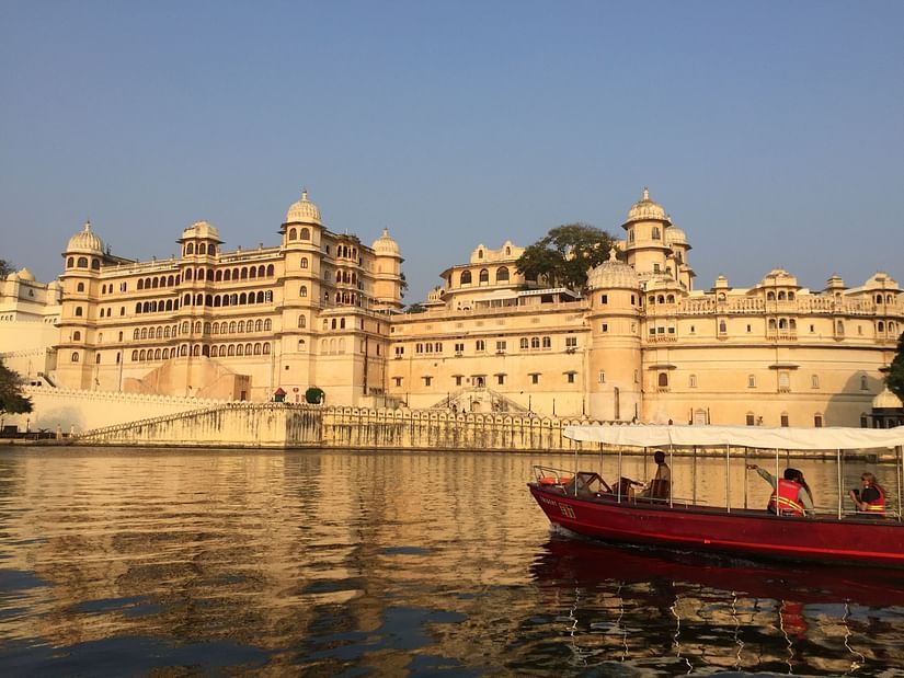 Udaipur palace in all its glory next to a lake with a boat holding people travelling on the lake