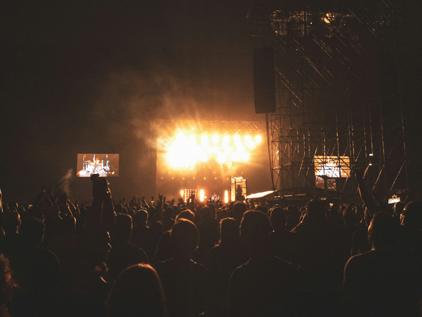 Large crowd gathered before a brightly lit concert stage during an outdoor night-time music event