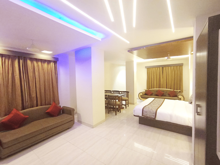 Suite room featuring bright linear ceiling lights, a brown couch, and a bed in the background.