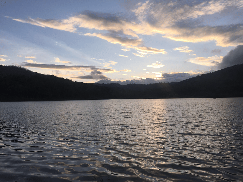 Calm lake surrounded by rolling hills under a colourful sunset sky, creating a peaceful and scenic landscape.