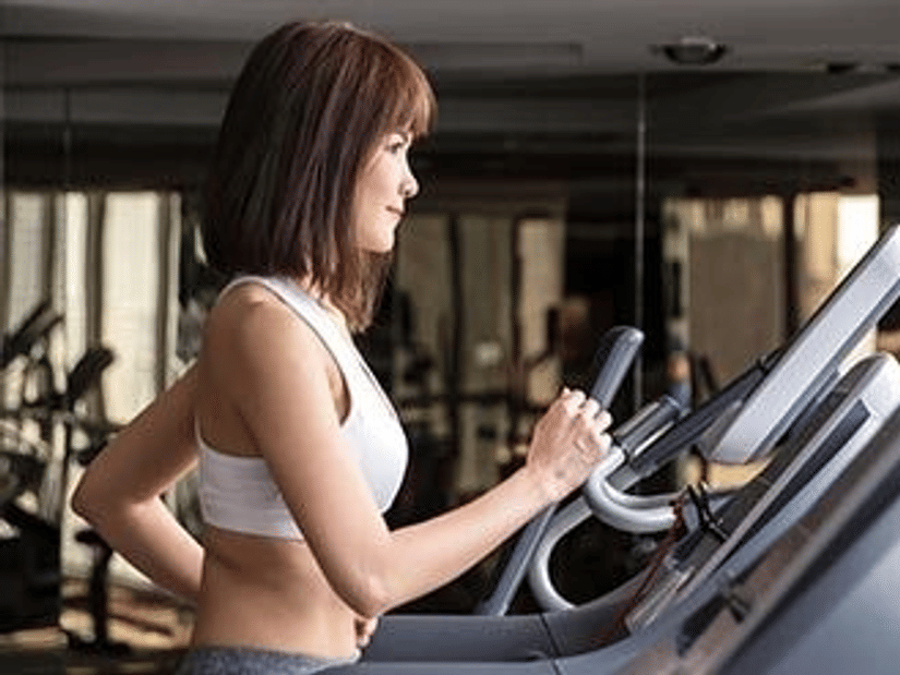 A woman in a white sports top working out on a cardio machine in a gym