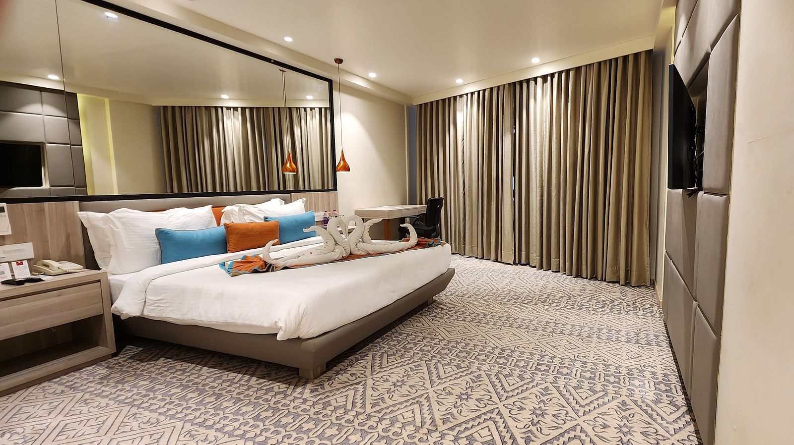 Luxurious bedroom with a large double bed, mirrored wardrobe, floor-to-ceiling curtains, and soft lighting.