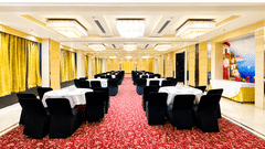 Reception area at Golden Tulip Kukas Jaipur featuring a white front desk, ornate dark patterned wall, marble floors, and warm overhead lighting.