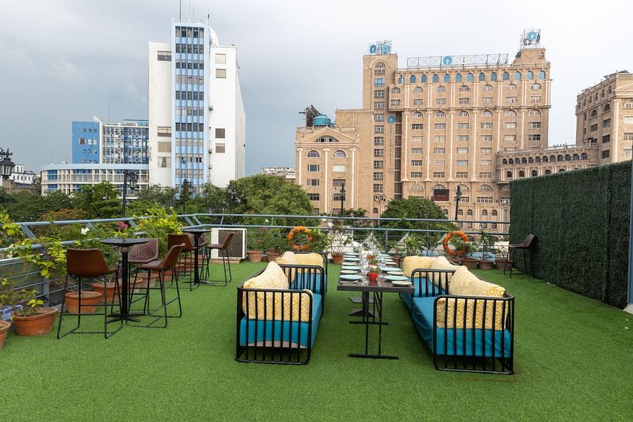 A rooftop garden cafe with artificial grass, potted plants, and a view of an ornate building in the background. - Polo Floatel, Kolkata