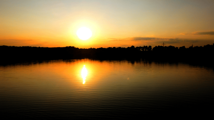 The sun setting over lake with it being reflected on still water, creating a clear horizon view.
